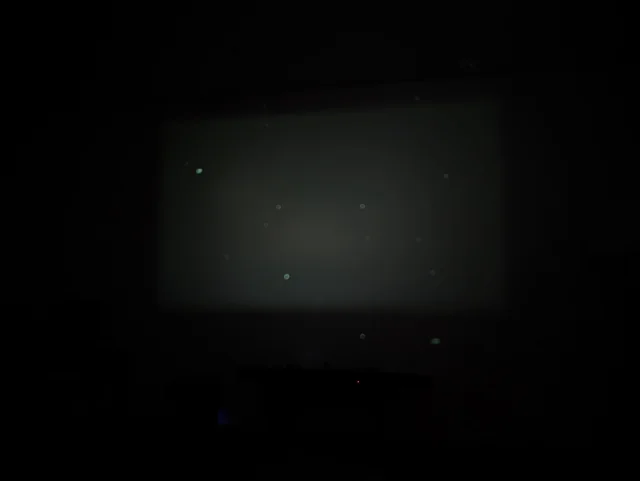 Tela de projeção escura com várias manchas circulares claras indicando acúmulo de poeira na lente ou LCD.