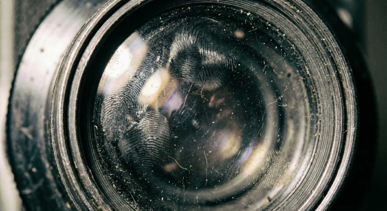 Lente de projetor suja com marcas de dedos e poeira acumulada, prejudicando a qualidade da imagem.